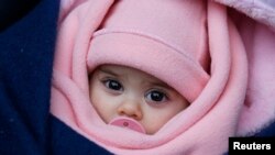 Seorang balita terbungkus selimut bersama orang tuanya di stasiun kereta di Presevo, Serbia, 19 Januari 2016. REUTERS/Marko Djuric
