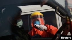 A worker in a protective suit checks the temperature of a truck driver as the country is hit by an outbreak of the novel coronavirus, in Beijing, China, Feb. 19, 2020. 