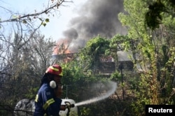 Seorang petugas damkar berupaya memadamkan api yang membakar sebuah rumah saat kebakaran hutan melanda desa Varnava, dekat Athena, Yunani, 11 Agustus 2024. (Michalis Karagiannis/Eurokinissi via REUTERS)