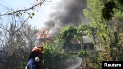 Seorang petugas damkar sedang memadamkan api yang membakar sebuah rumah yang dilalap kebakaran hutan di desa Varnava dekat Athena, Ibu Kota Yunani, Minggu, 11 Agustus 2024. (Foto: Michalis Karagiannis/Eurokinissi via Reuters)