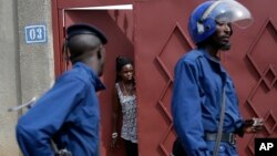 FILE - A resident looks out of house as riot police walk past in Bujumbura's Nyakabiga district in Burundi, May 4, 2015. 