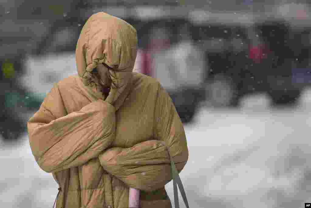 A woman uses her winter clothes to shield from the wind and snow on a street as the capital is hit by snowstorm in Beijing, China.