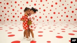 Wearing matching dresses, Takara Thomas, 3, left, and Noemi Vega, 4, hug in a polka-dotted room created by Japanese artist Yayoi Kusama, part of the installation called "With All My Love for the Tulips, I Pray Forever" at the Marciano Art Foundation in Lo