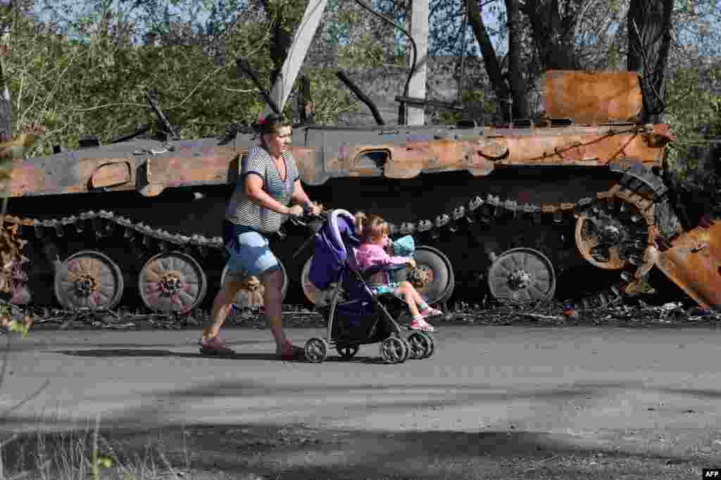 A woman pushes a girl in a stroller past a destroyed armored vehicle left behind by the Ukrainian army in Lutuhyne, some 20 km south of Lugansk, Ukraine.