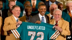 El exmariscal de campo de los Dolphins, Bob Griese (izquierda) y el entrenador, Don Shula, entregan al presidente Obama una playera autografiada por los jugadores invictos en 1972.