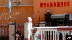 新疆喀什地區伽師縣一所小學校門有鐵絲網和監控鏡頭，校門前寫著：請使用國家通用語言。 （2018年8月31日）