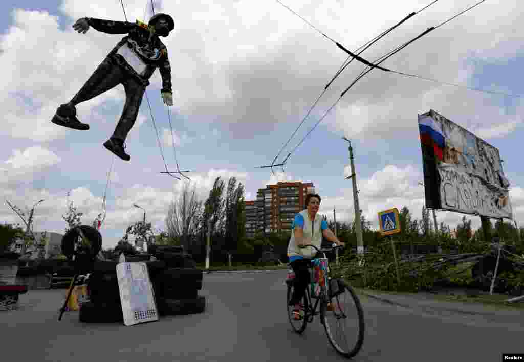 An effigy of a Ukrainian soldier hangs above a pro-Russian checkpoint as a local woman cycles by the entrance of the eastern Ukrainian town of Slovyansk, May 13, 2014.