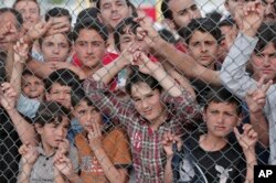 FILE - Migrants stand behind a fence at the Nizip refugee camp in Gaziantep province, southeastern Turkey, April 23, 2016.