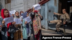 FILE - A Taliban fighter watches as Afghan women hold placards during a demonstration demanding more rights for women, in front of the former Ministry of Women Affairs in Kabul, Afghanistan, Sept. 19, 2021. 