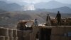 FILE - Afghan local police officials look on as smoke rises after an airstrike on Islamic State militant positions in a checkpoint at the Deh Bala district in the eastern province of Nangarhar province, July 7, 2018.