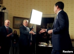 El presidente de EE.UU., Donald Trump, saluda al director del FBI James Comey mientras el director del Servicio Secreto Joseph Clancy (L), observa durante una recepción a oficiales de la ley y paramédicos en el salón azul de la Casa Blanca el 22 de enero de 2017.