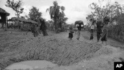 Cambodian villagers walk around bomb crater in a road near embattled Takeo 42 miles southwest of Phnom Penh in Cambodia May 17, 1973.