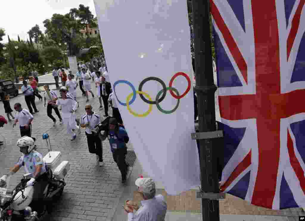 A Union flag and an Olympic flag are seen as Chris Theodoropoulos, a Greek student who plays basketball for a local team, runs with the Olympic flame during the Olympic torch relay.