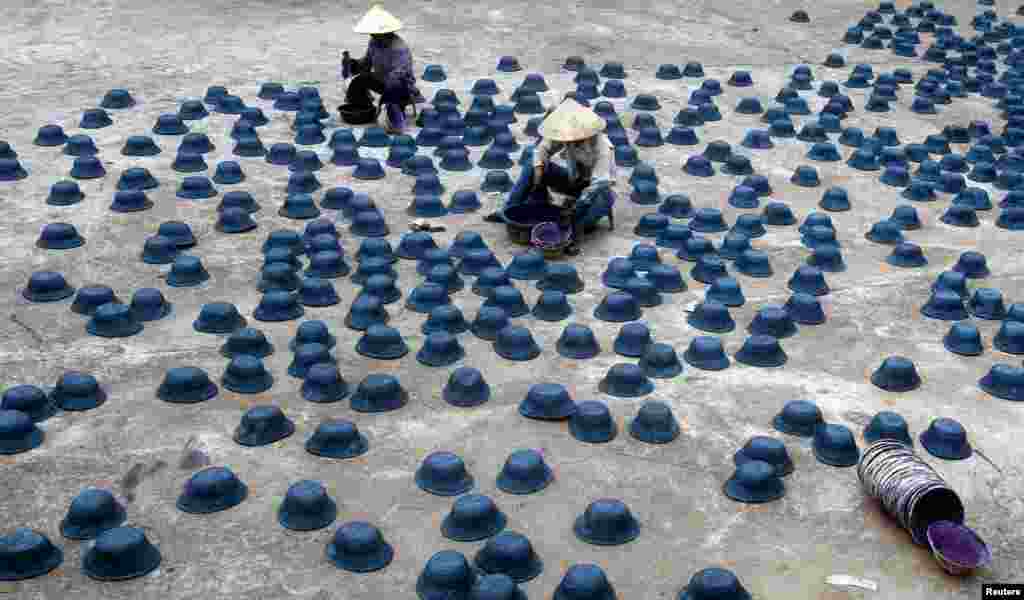 Dua perempuan mengecat topi-topi tentara dalam festival Vu Lan (Hantu Lapar) yang berlangsung sebulan di Hanoi.