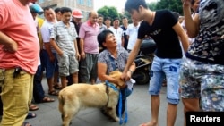 Seorang aktivis penyayang binatang (tengah) memohon agar seekor anjing yang dipegangnya tidak dibunuh untuk dikonsumsi dalam festival tahunan di Yulin, wilayah Guangxi Zhuang, dengan menawarkan untuk membelinya dari seorang penjual (dua dari kanan) (Foto: dok). 