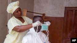 A healthcare worker, left, helps a colleague as she prepares his Ebola personal protective equipment before entering the Ebola isolation ward at Kenema Government Hospital, in Sierra Leone, Aug. 12, 2014.