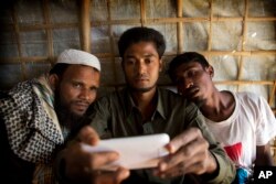 Rohingya Muslim refugee Mohammad Karim, 26, center, shows a mobile video of Gu Dar Pyin's massacre to other refugees in Kutupalong refugee camp, Bangladesh, Jan. 14, 2018.