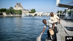 Les survivants tutsis du massacre de Bisesero, Eric Nzabihimana (à gauche) et Bernard Kayumba, déversent de la terre de Bisesero dans la Seine, à Paris, le 26 juin 2019.