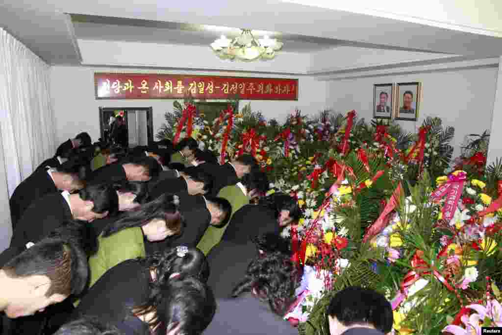 Warga Korea Utara menyimpan karangan bunga dan pita di depan potret-potret Kim Il Sung dan Kim Jong Il saat mereka memperingati dua tahun kematian Kim Jong Il di Kedutaan Besar Korea Utara di kota perbatasan China, Dandong (17/12). 