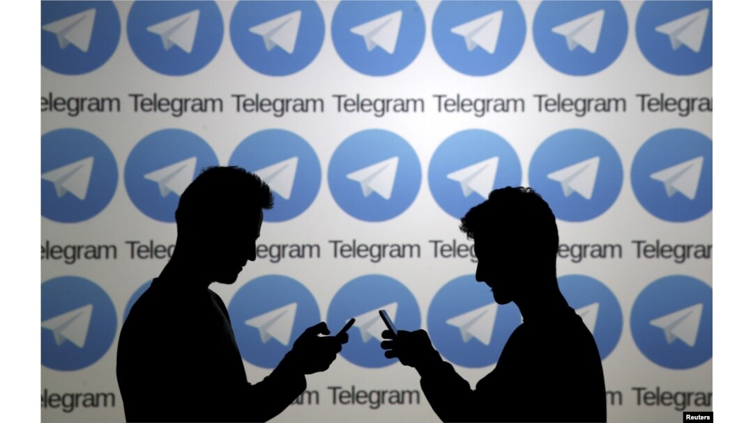 FILE - Two men pose with smartphones in front of a screen showing the Telegram logos in this picture illustration taken Nov. 18, 2015.