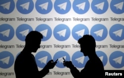 FILE - Two men pose with smartphones in front of a screen showing the Telegram logos in this picture illustration taken Nov. 18, 2015.