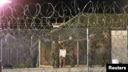 FILE - Marines at Camp X-Ray at the Naval Base at Guantanamo Bay, Cuba escort a newly arriving detainee into a processing tent after being showered.