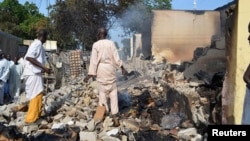 FILE - Residents watch as two men walk amidst rubble after Boko Haram militants raided the town of Benisheik, west of Borno State capital Maiduguri, Nigeria, Sept. 19, 2013.