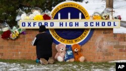 A well wisher kneels to pray at a memorial on the sign of Oxford High School in Oxford, Mich., Dec. 1, 2021.