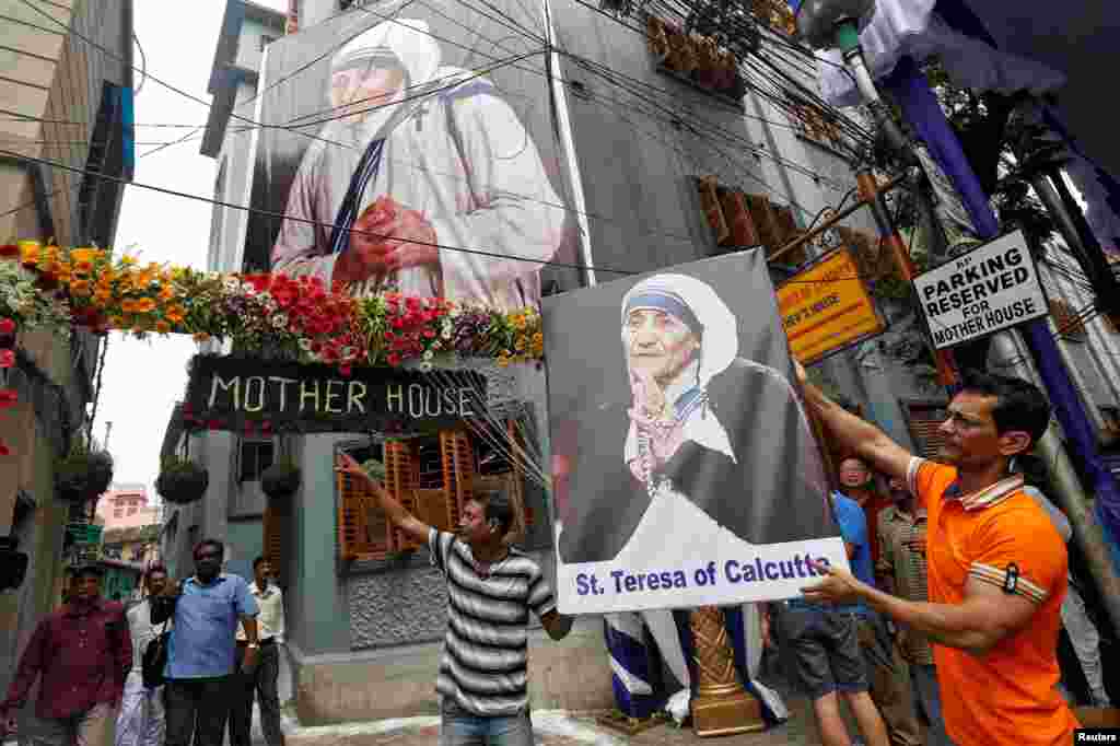 Homem carrega cartaz com a imagem da Madre Teresa junto ao edificio das Missionárias da Caridade em Calcutá.