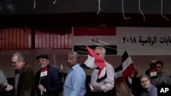 Egyptian men wave national flags as they wait in line to vote during the first day of the presidential election in front of a polling site in Cairo, Egypt, Monday, March 26, 2018.