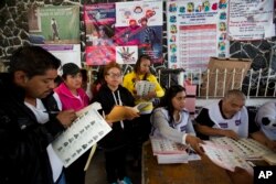 An election worker hands a ballot to a voter as observers from political parties mark off each voter from copies of the rolls in Chimalhuacan, Mexico state, June 4, 2017.