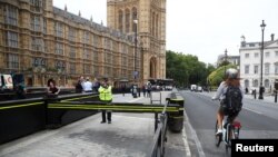 A cyclist passes a police officer standing at the vehicle barrier to the Houses of Parliament where a car crashed after knocking down cyclists and pedestrians the day before in Westminster, London, England, Aug. 15, 2018.
