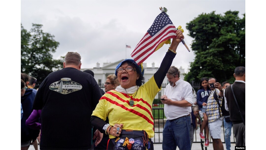 Victoria Kim, a Vietnamese Trump supporter from California, raises an American flag during a vigil outside the White House June 11, 2018, to celebrate the joint summit between U.S. President Donald Trump and North Korean leader Kim Jong Un in Singapore.