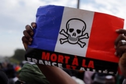 FILE - A supporter holds a flag of France, with the drawing of a skull on it, during a demonstration called by Mali's transitional government, in Bamako, Mali, Jan. 14, 2022. The flag reads "Death to France and allies."