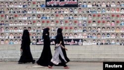 FILE - Shi'ite Muslim women walk past a wall with portraits of the deceased, who were killed in a bombing in a residential area in March 2013, during the Shi'ite Youm Ali procession in Karachi, Pakistan, June 27, 2016. 