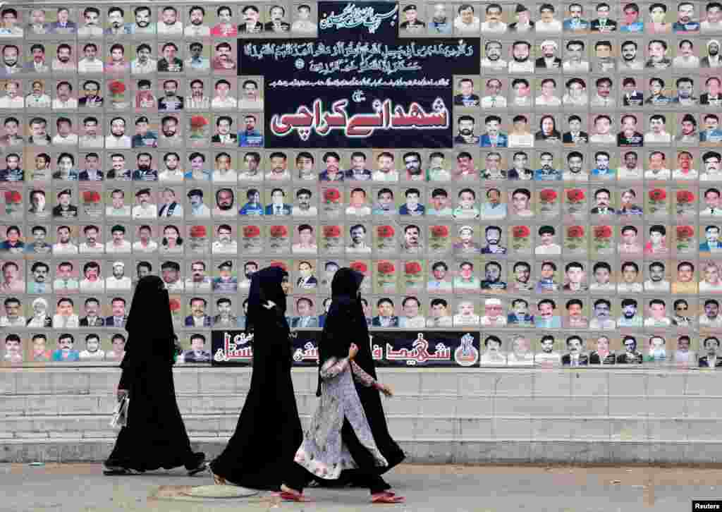 زنان در حال عبور از مقابل دیوار یادبود از قربانیان بمگذاری ماۀ مارچ سال ۲۰۱۳ در محلۀ شیعه نشین شهر کراچی پاکستان.