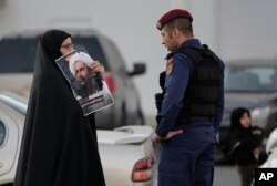 A Bahraini protester holds up a picture of Saudi Shi'ite cleric Sheikh Nimr al-Nimr in front of a riot police officer in Daih, a largely Shi'ite suburb of the capital, Jan. 4, 2016.