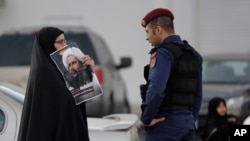 Mwanamke wa Bahrain akishikilia picha ya kiongozi wa kishia aliyenyong'wa, Sheikh Nimr al-Nimr mbele ya polisi wa kutuliza ghasia, Jan. 4, 2016. 