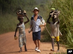 FILE - Children living in a cocoa-producing village walk back from the fields carrying wood and food stuffs on their heads on the outskirts of the town of Oume, Ivory Coast, June 30, 2005.