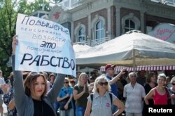 FILE - People attend a rally against planned retirement age hikes, in Krasnodar, Russia, Sept. 9, 2018. The poster at left reads: "Pension age hike amounts to lifetime slavery."