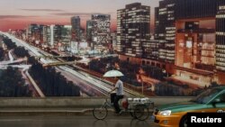 Un homme passe en tricycle devant une affiche publicitaire montrant une vue nocturne de la ville sur le chantier de construction d'une tour d'appartements à Pékin, le 19 juillet 2016.