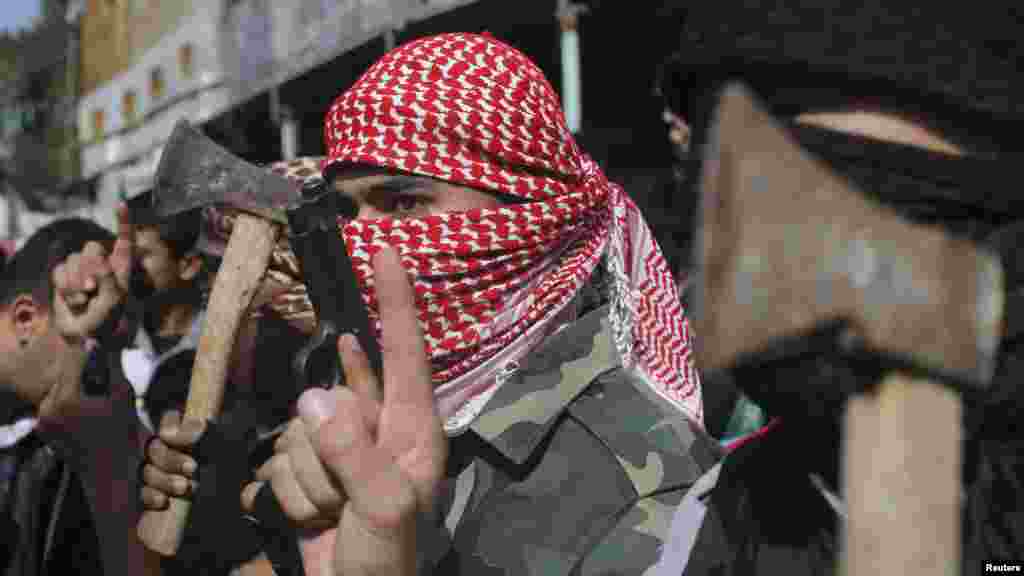 Palestinianos com máscaras seguram em machados e numa arma festejando o ataque à sinagoga em Jerusalém, Rafah, sul da Faixa de Gaza, Nov. 18, 2014.