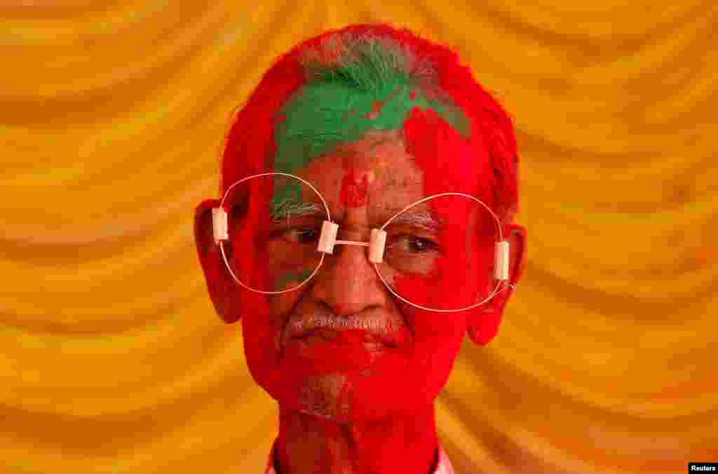 A man, with his face daubed in colors, wears eye frames made of bamboo straw during Holi celebrations in Chennai, India.