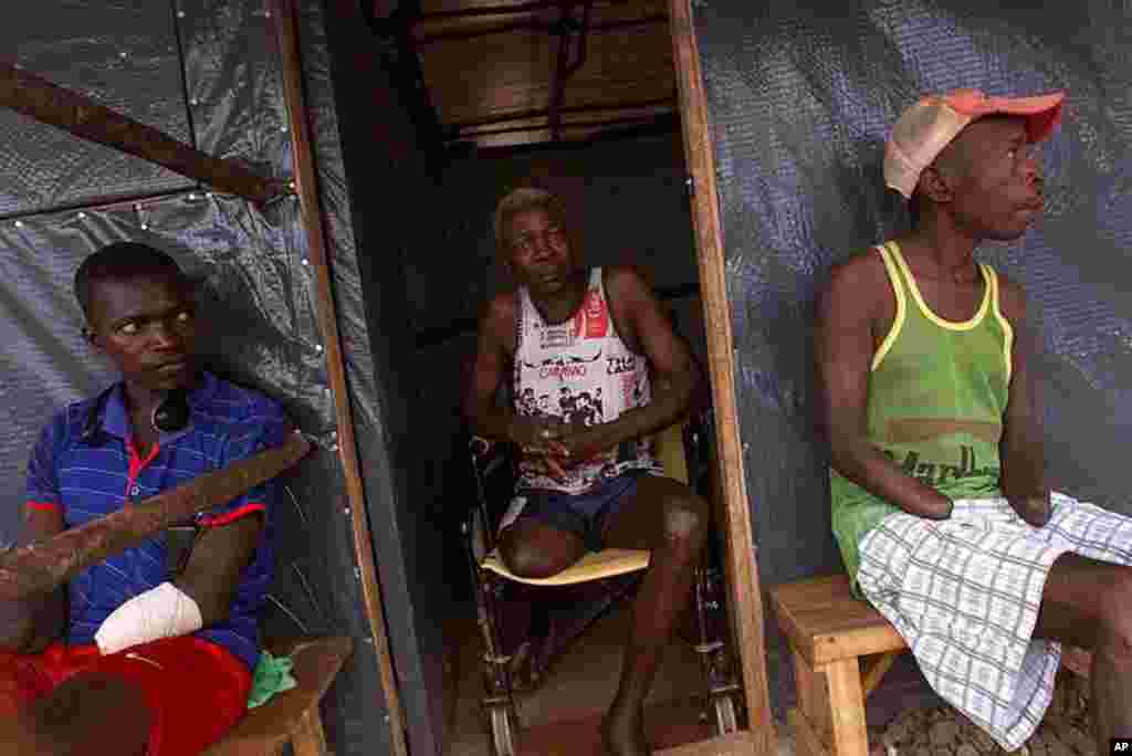 Sierra Leonean Nethaniel Bemeh, 72, center, who said his leg was shot off at point blank range by terrorist rebels, sits with his neighbors Abubakar Karbu, left, and David Kaiwo, right, who had hands chopped off by rebels, in front of their plastic shelte