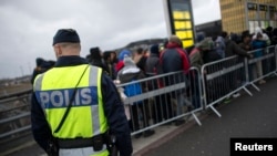 FILE - A police officer keeps guard as migrants arrive at Hyllie station outside Malmo, Sweden.