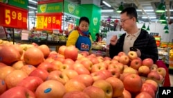 FILE - a woman wearing a uniform with the logo of an American produce company helps a customer shop for apples a supermarket in Beijing. 