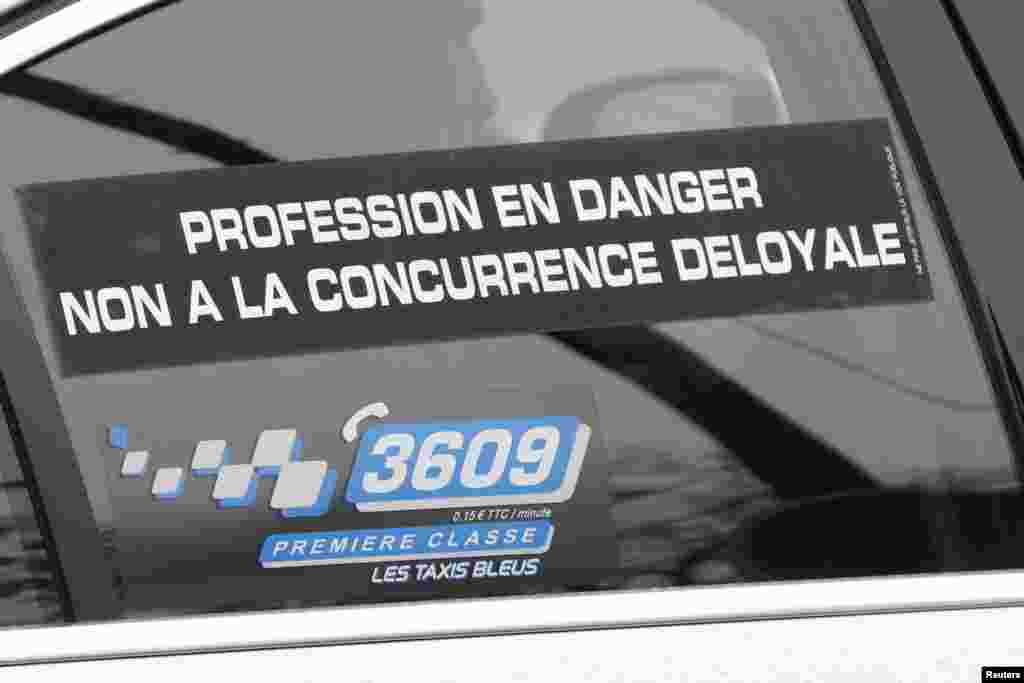 A striking Paris taxi displays a sign reading "Profession in danger, No to unfair competition" during a demonstration over the Paris ring road, Dec. 15, 2014.