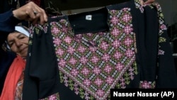 In this Monday, January 28, 2019 photo, Samiha Jeheshat, displays a handmade embroidered Palestinian thobe at her showroom in the West Bank village of Idna, north of Hebron.