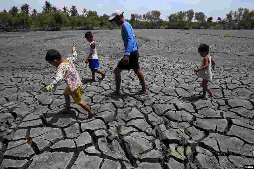 A father and his children walk over the cracked soil of a 1.5 hectare dried up area in the Novaleta town in Cavite province, south of Manila, the Philippines.