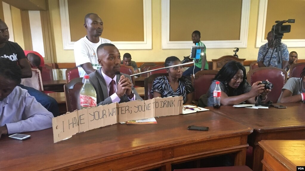 A Harare resident displays a sample of dirty water in a bottle next to him during a meeting with the city's mayor at a meeting at Town House, in Harare, Zimbabwe, Dec. 29, 2017. (S. Mhofu/VOA)